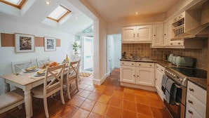 A kitchen with white cabinets, a stove, and a dining area with a table and chairs. - Cotswolds   2BD   1 Bath   Garden   City Centre (Gloucestershire)