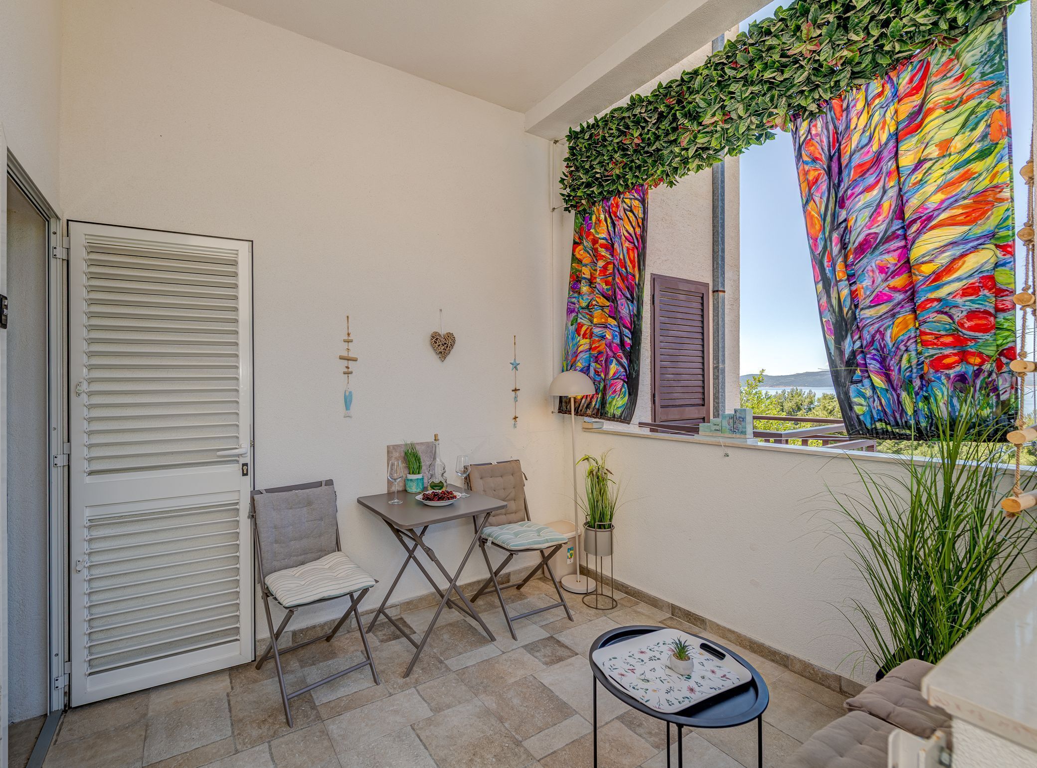 A balcony with a table, chairs, a potted plant, and a colorful curtain.