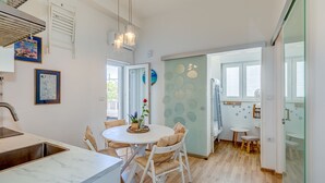 Moderni keittiö, jossa on ruokailutila, sisäänrakennettu ilmastointilaite ja näkymä avoimesta ovesta lastenhuoneeseen.