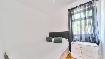 A bedroom with a bed, a bedside table, a lamp, and a window with sheer curtains.