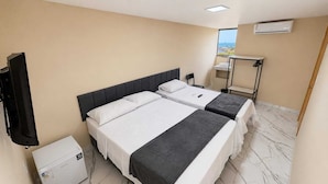Habitación de hotel con dos camas, televisión, escritorio pequeño, estante y ventana con vistas.