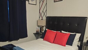 Een bed met een zwart hoofdbord, een witte matras en rode en blauwe kussens.