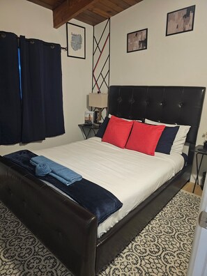 A bed with a black headboard, a white mattress, and red and blue pillows. - PNSUITES -SHARED FACILITIES-NEWLY RENOVATED (CLEANLINESS, COMFORT,AFFORDABILITY) (Edmonton)