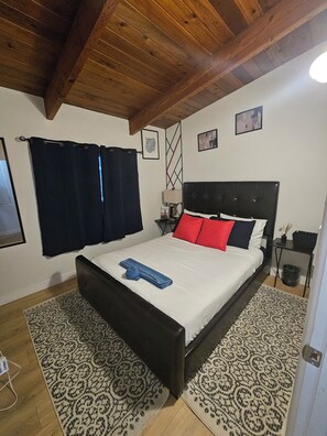 A bedroom with a bed, dark curtains, a headboard, a nightstand, a lamp, and a wall with framed pictures. - PNSUITES -SHARED FACILITIES-NEWLY RENOVATED (CLEANLINESS, COMFORT,AFFORDABILITY) (Edmonton)