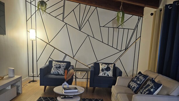 Een moderne woonkamer met een geometrisch wandontwerp, twee banken met gestreepte kussens, een salontafel en een bijzettafeltje.