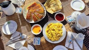 A meal setup with various dishes including bread, eggs, and a drink, arranged on a table outdoors.