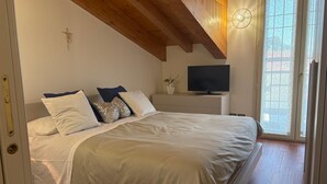 Un dormitorio con cama, almohadas, televisor, planta y ventana.