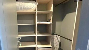 Ein begehbarer Kleiderschrank mit mehreren Regalen und Schubladen, einem Handtuchhalter und einem waschmaschinenmaschinenartigen Duschvorhang.
