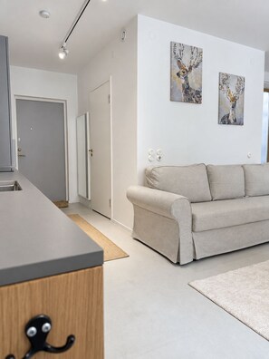 A modern living room with a sofa, a kitchen area, and artwork on the wall. - Luxury Two-Story Apartment in the Heart of Stockholm (Stockholm)