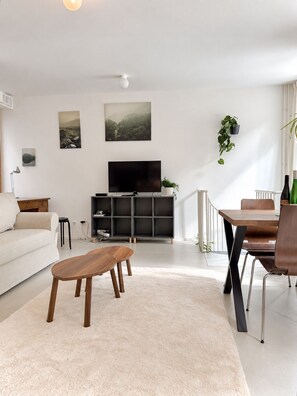 A modern living room with a sofa, a wooden coffee table, a TV on a black stand, and a dining area with chairs and a table. - Luxury Two-Story Apartment in the Heart of Stockholm (Stockholm)