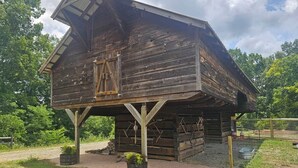 A rustic wooden barn with a slanted roof, a wooden door, and a fenced area with a gravel path. - Southern Charm (Sevierville)