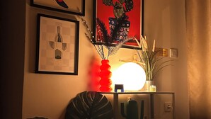 Una habitación con una estantería de pared que sostiene una lámpara, una obra de arte enmarcada y una planta de cactus.