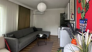 Una sala de estar moderna con un sofá gris, una mesita redonda pequeña, un ventilador de techo blanco y una pared roja con una pintura de un cactus.