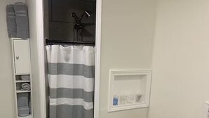 Casa de banho com chuveiro, sanita e um pequeno armário com produtos de higiene pessoal.