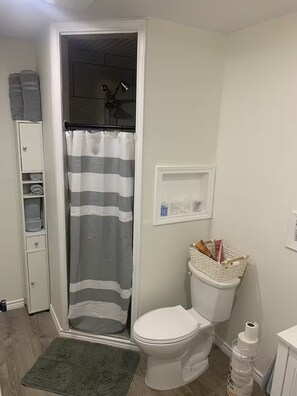 A bathroom with a shower, toilet, and a small shelf with toiletries. - Welcome to Lilly's Pad (Aquilla)