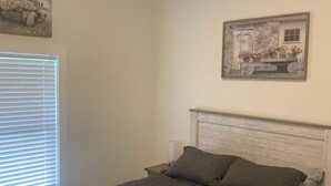 Quarto com cama, mesa de cabeceira, janela com persianas e ventilador de teto.