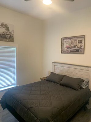 A bedroom with a bed, a nightstand, a window with blinds, and a ceiling fan. - Welcome to Lilly's Pad (Aquilla)