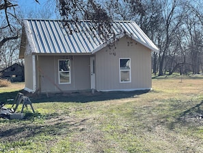 A small, single-story building with a sloped metal roof, two windows, and a door. - Welcome to Lilly's Pad (Aquilla)