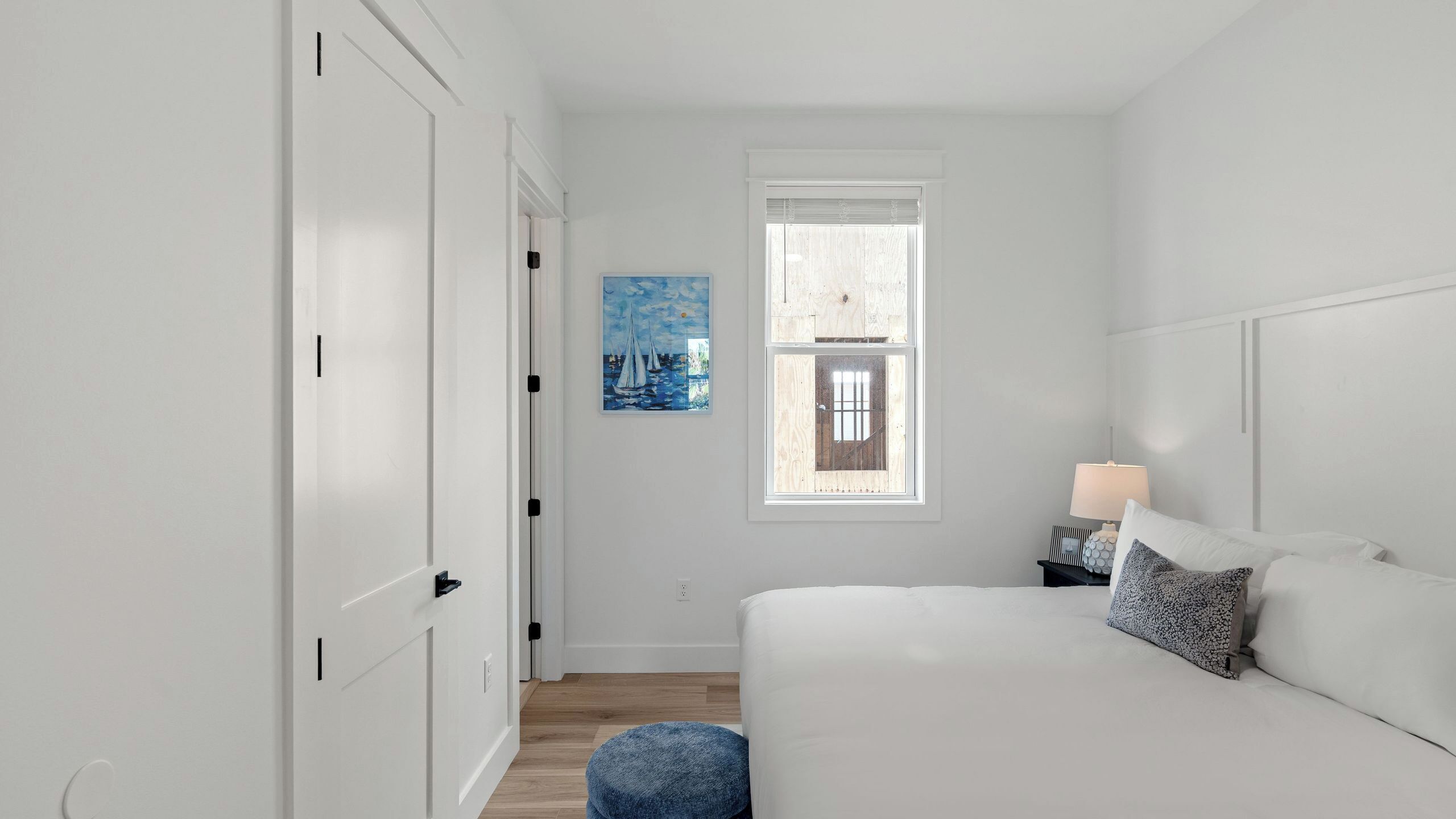 Ein Schlafzimmer mit einem Bett, einem Nachttisch, einer Lampe, einem Gemälde und einem Fenster.