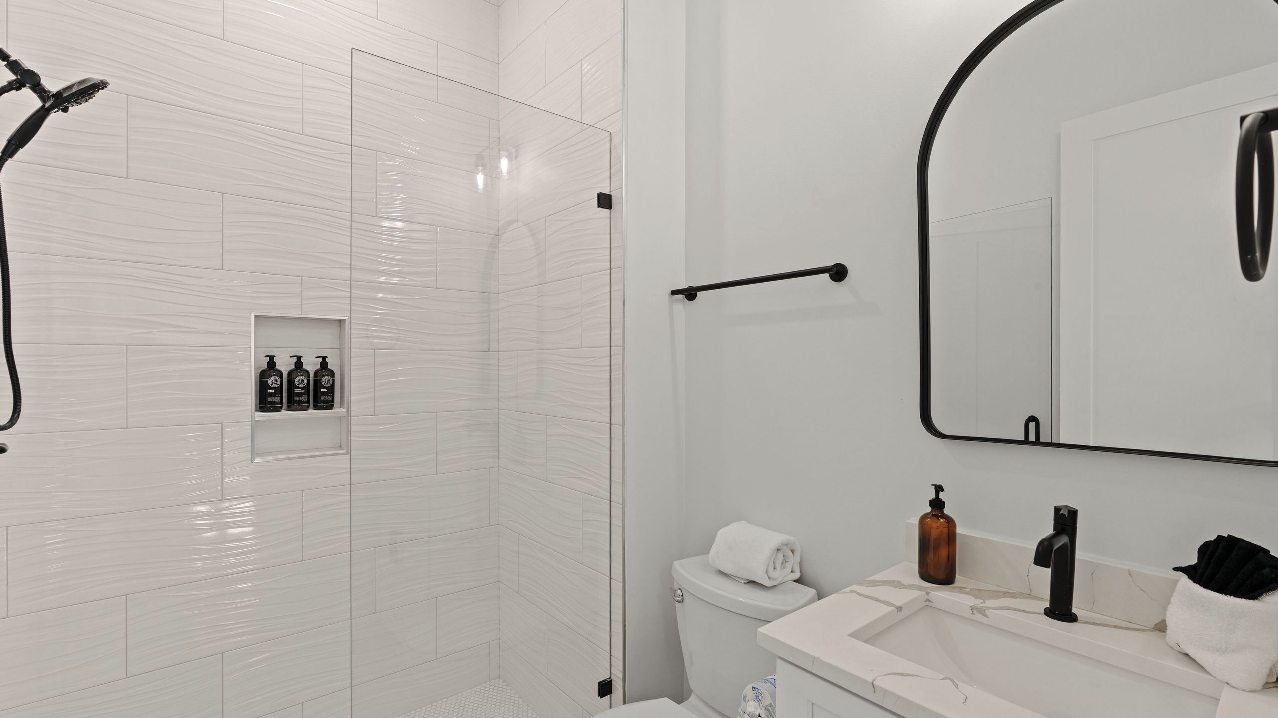 A bathroom with a shower, toilet, sink, and mirror.
