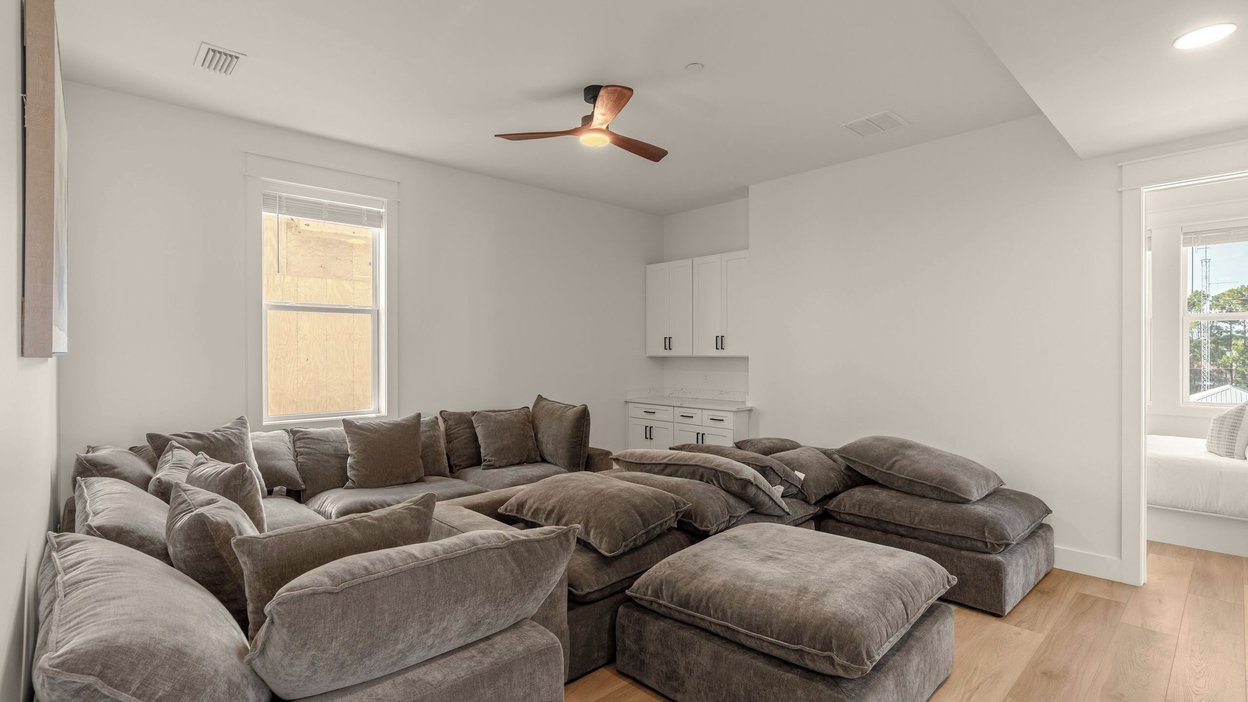 Een moderne woonkamer met een modulaire bank, een plafondventilator en uitzicht op buiten.