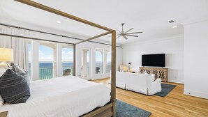 Une chambre moderne avec un lit à baldaquin, un canapé, une télévision et un balcon offrant une vue sur la mer.