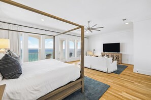 Ein modernes Schlafzimmer mit einem Himmelbett, einer Couch, einem Fernseher und einem Balkon mit Meerblick.