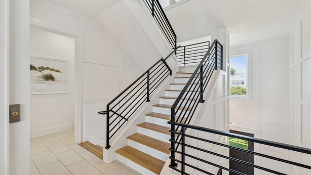 Un escalier avec des rampes noires et des marches en bois, menant à un palier où se trouvent une porte et une fenêtre.