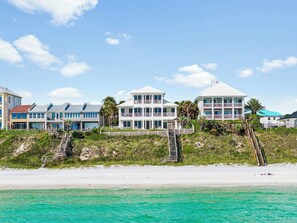 Ein Strandgrundstück mit mehreren Gebäuden, darunter ein großes Hauptgebäude mit Balkonen und ein kleineres Gebäude links.