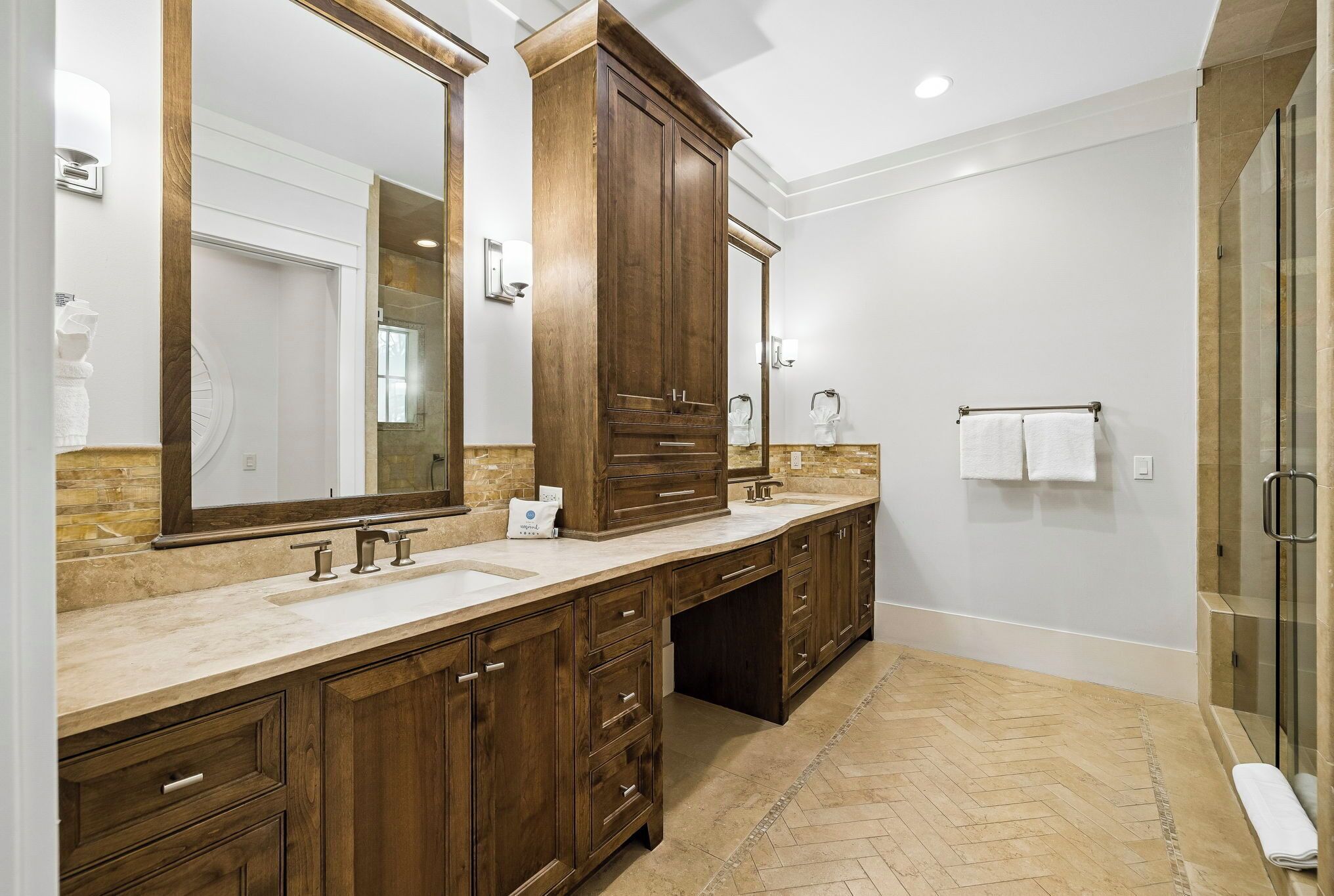 Your private spa-like bathroom features dual vanities with elegant stone countertops, rich wood cabinetry, and a spacious walk-in shower. Fresh towels and thoughtful touches await your arrival.