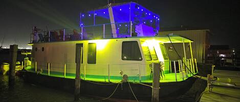 A stationary boat with a cabin, deck area, and a covered section with lights.