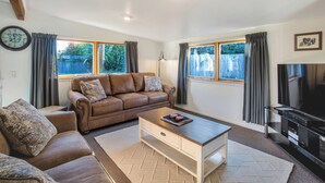 A living room with a brown leather sofa, a wooden coffee table, a TV, and large windows with curtains.