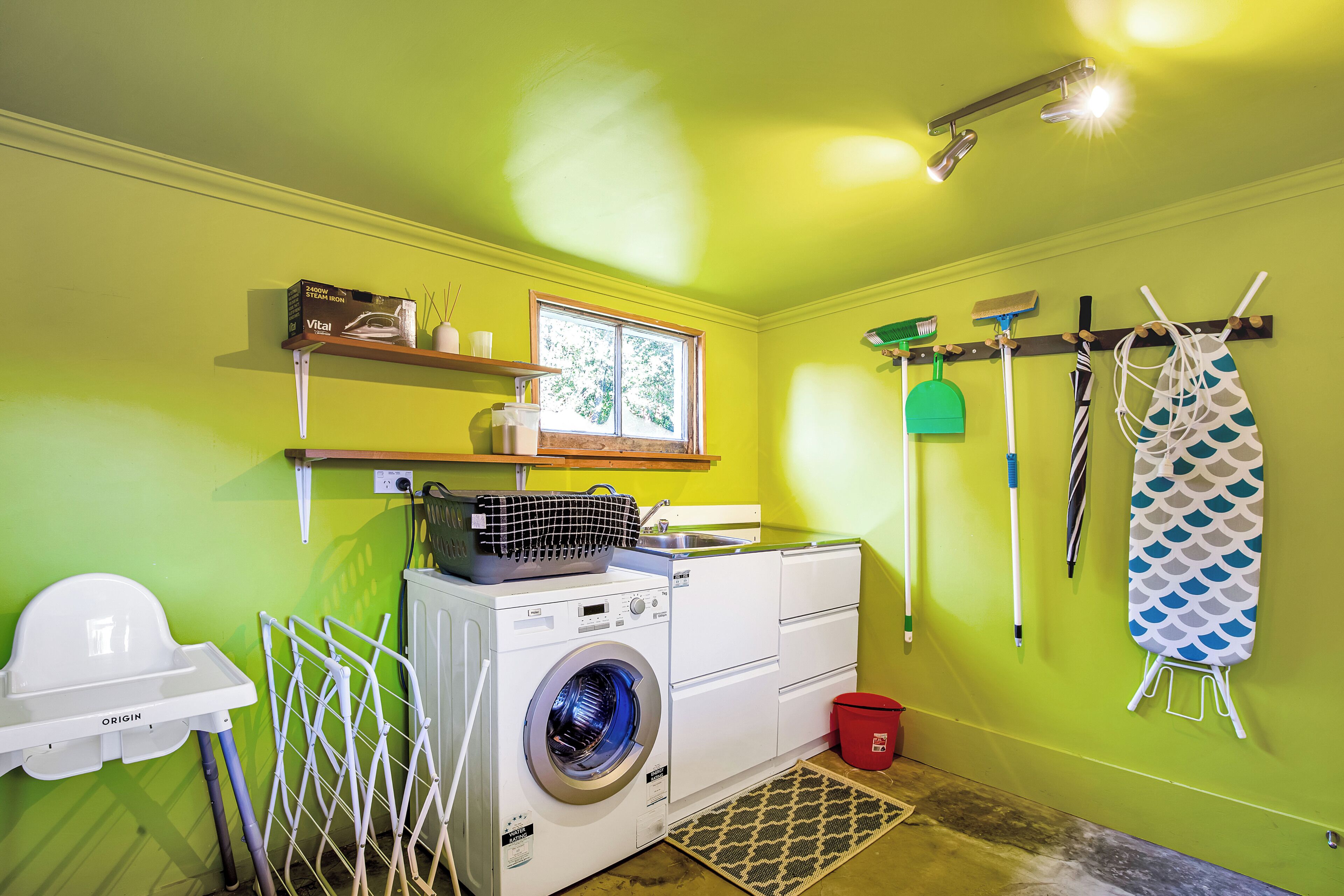 A laundry room with a washing machine, drying rack, and ironing board.