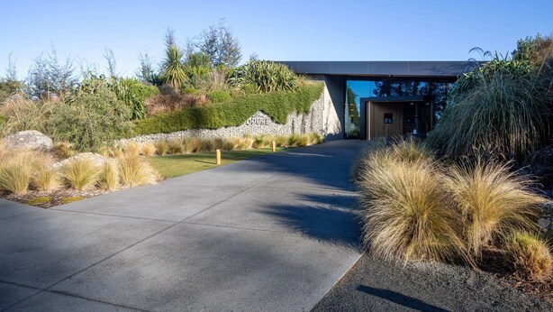 A modern building with a concrete pathway leading to a wooden entrance.