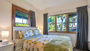 A bedroom with a bed, nightstand, lamp, and windows with curtains.