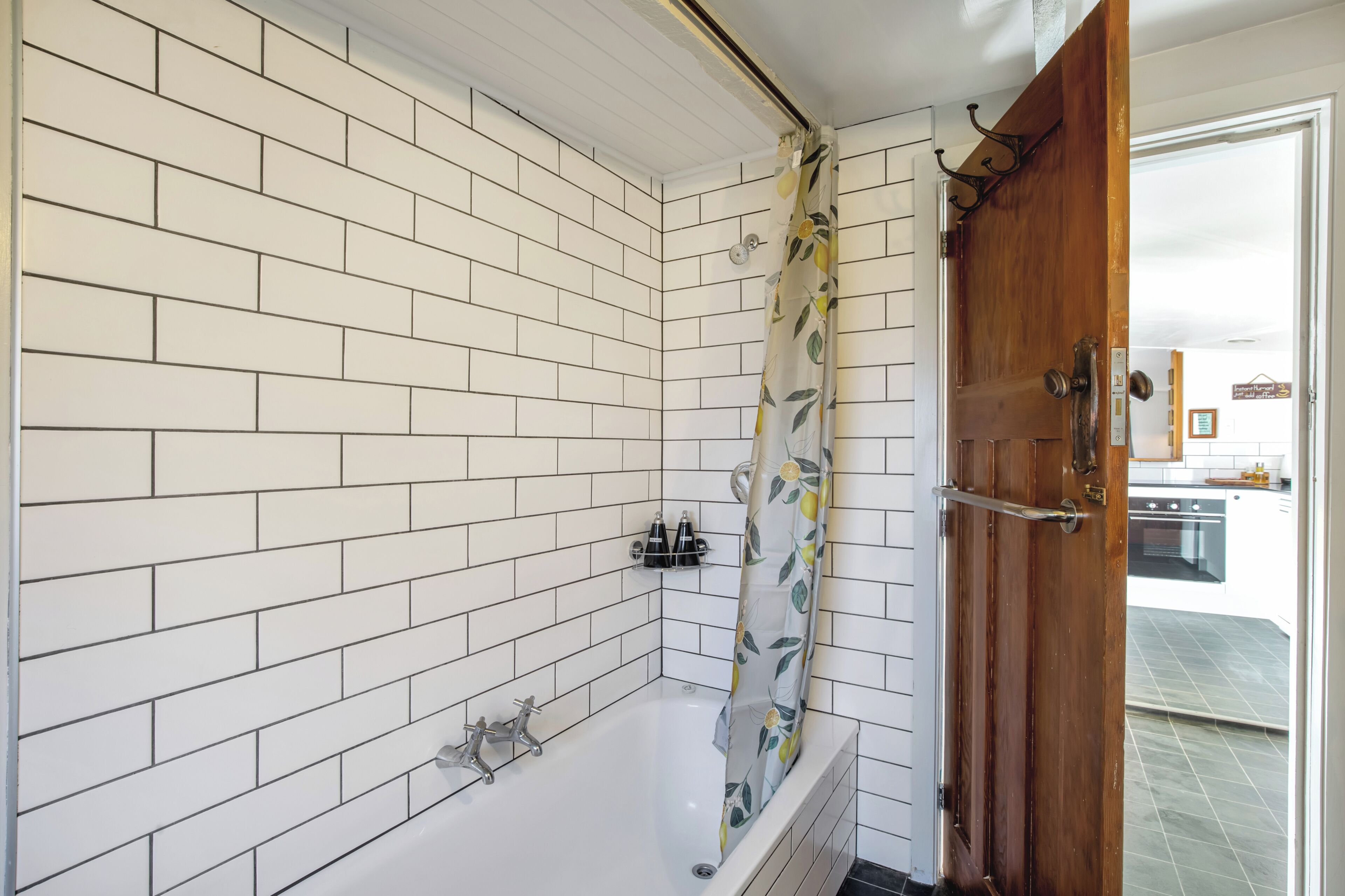 Une salle de bain avec des murs carrelés de carreaux blancs, une douche avec un rideau à motifs floraux et une porte en bois.