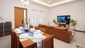 Uma sala de estar moderna com área de jantar, sofá, televisão e um aparador de madeira.