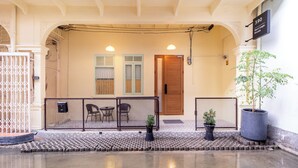 Entrada de um edifício com porta de madeira, placa indicando '390 Heritage House' e uma pequena área externa com cadeiras e mesa.