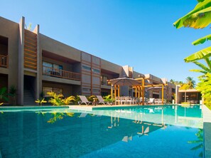 Un hotel con piscina, tumbonas y una zona de estar cubierta.