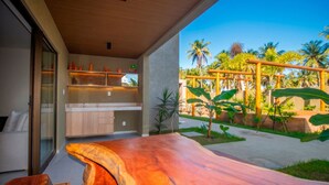 A modern kitchen with a large island, a glass door leading to a balcony, and a view of a tropical garden. - Azuk Milagres 6 p Close to Patacho Beach by MME (Porto de Pedras)