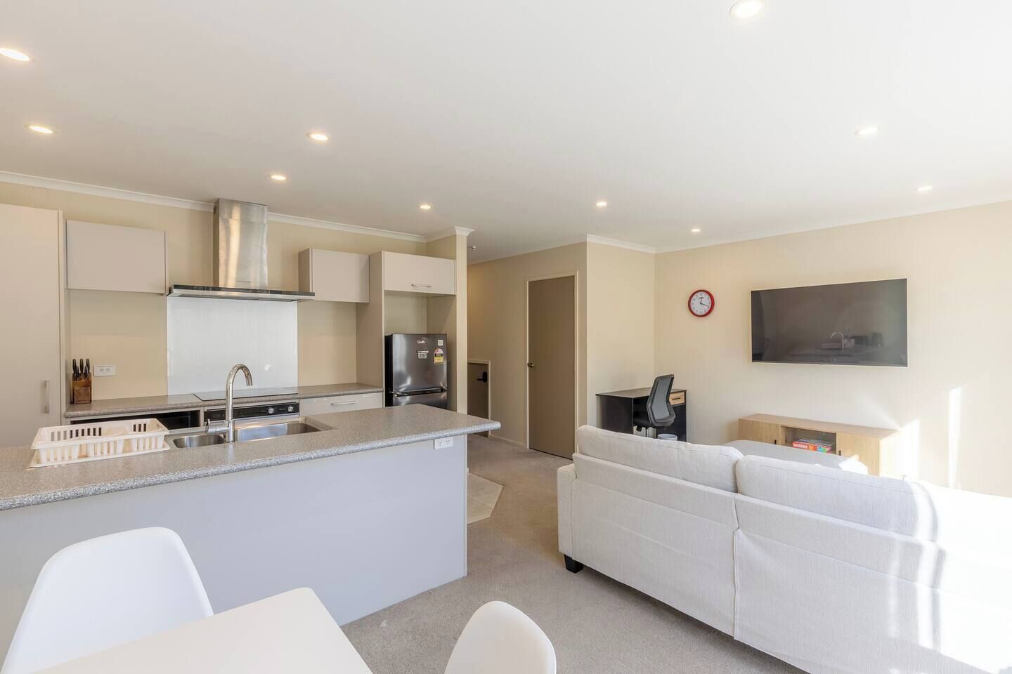 Una cocina moderna con una isla central, un comedor con una mesa y sillas blancas, una sala de estar con un sofá y un televisor de pantalla plana montado en la pared.