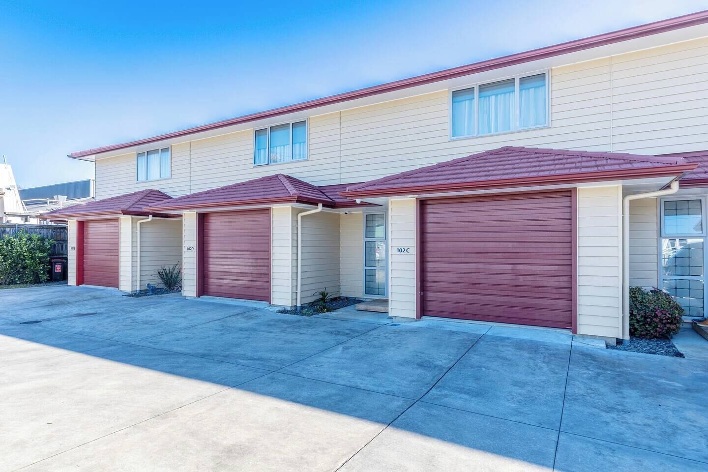 Une rangée de maisons de ville avec des portes de garage rouges, un revêtement de couleur beige et un ciel d’un bleu limpide.
