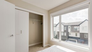 Een slaapkamer met een bed, een kledingkast en een raam met uitzicht op omliggende gebouwen.