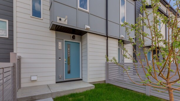 Een modern, tweelaags gebouw met een blauwe deur, een kleine boom in de voortuin en een grijze hek.