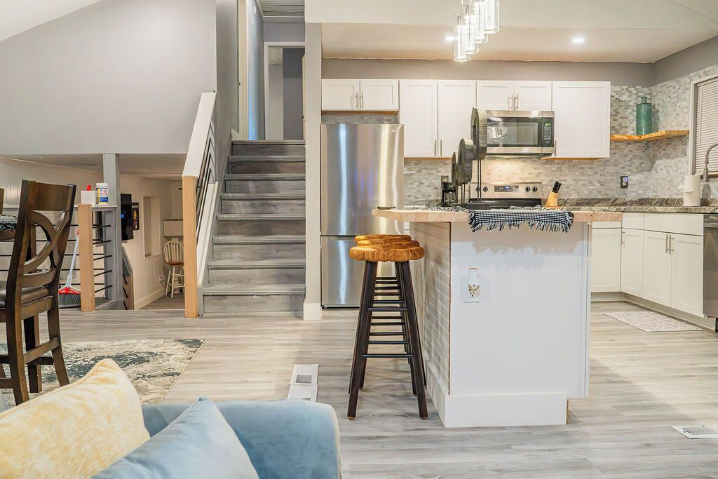 A modern kitchen with stainless steel appliances, a central island, and a staircase leading to an upper level.