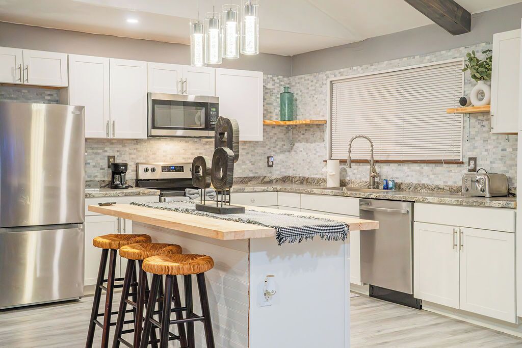 A modern kitchen with white cabinets, stainless steel appliances, a central island with stools, and a hanging light fixture.