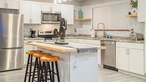 A modern kitchen with white cabinets, stainless steel appliances, a central island with stools, and a hanging light fixture. - Spacious Southern Charm with Pool Table! (Jonesboro)