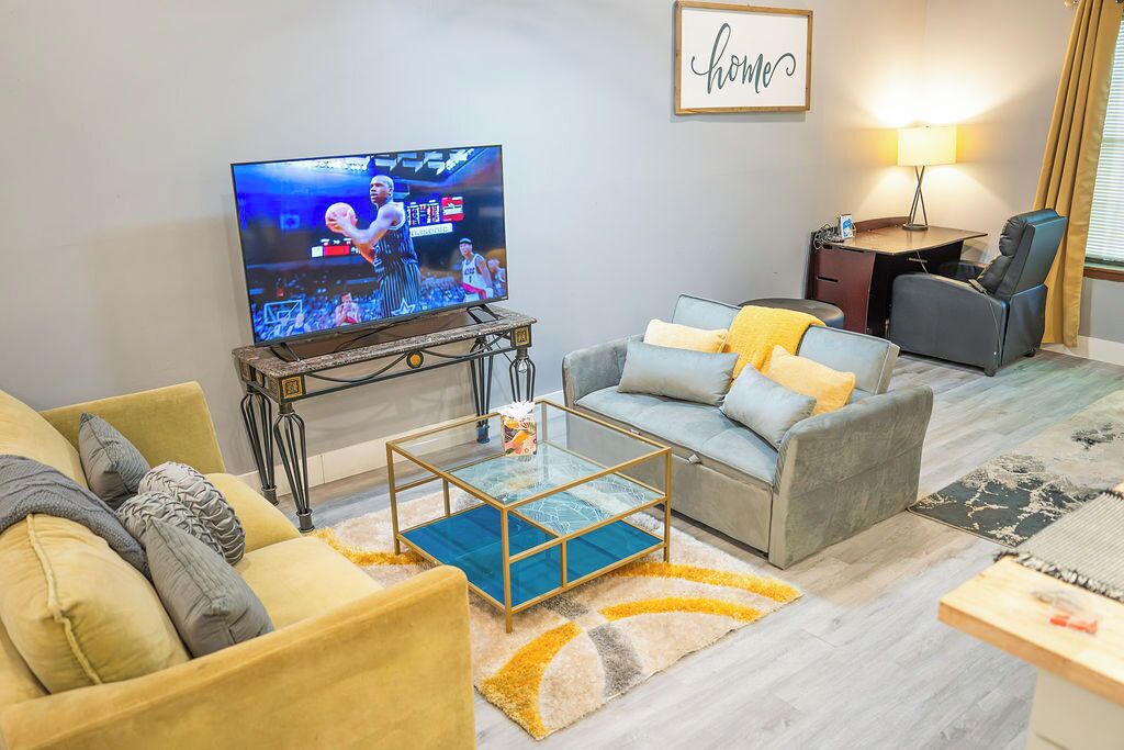A living room with a television, sofa, armchair, coffee table, and a desk with a lamp.