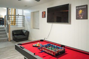 A pool table with a red felt surface, a black leather sofa, and a television mounted on the wall. - Spacious Southern Charm with Pool Table! (Jonesboro)