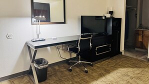 A hotel room with a desk, chair, TV, and a trash bin.